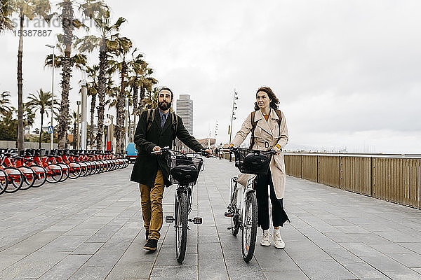Ehepaar schiebt E-Bikes an der Strandpromenade