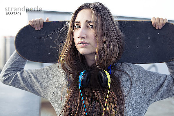 Porträt einer seriösen jungen Frau mit Skateboard und Kopfhörer