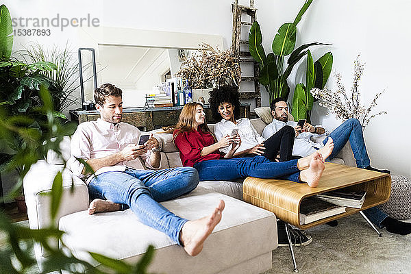 Freunde sitzen auf der Couch  arbeiten zwanglos zusammen  benutzen Smartphones