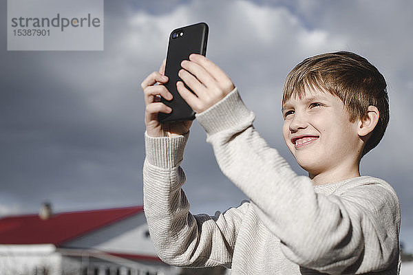 Porträt eines glücklichen Jungen  der sich mit einem Smartphone selbstständig macht