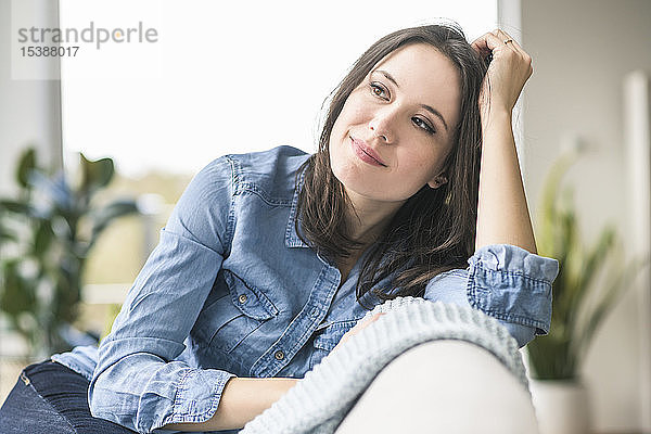 Porträt einer lächelnden Frau  die zu Hause auf der Couch sitzt