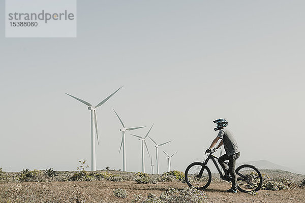 Spanien  Lanzarote  Mountainbiker auf einem Ausflug in die Wüstenlandschaft mit Windturbinen im Hintergrund