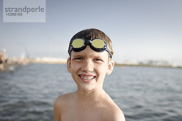 Porträt eines glücklichen Jungen mit Schwimmbrille am Meer