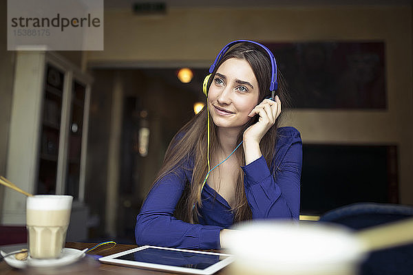 Entspannte junge Frau sitzt mit Kopfhörern in einem Café