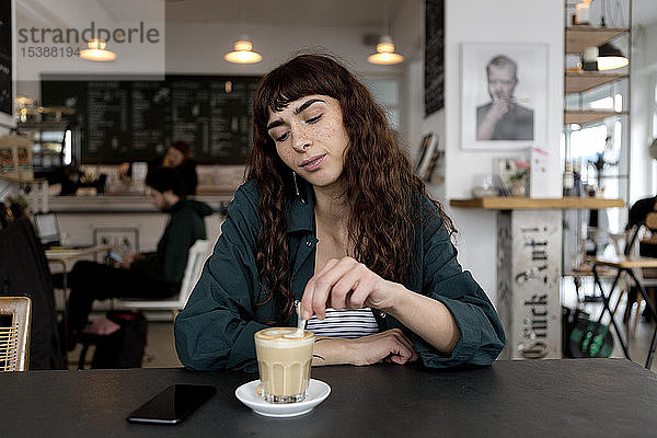 Junge Frau mit Milchkaffee  die in einem Café am Tisch sitzt