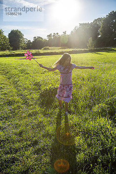 Glückliches Mädchen mit Windrädchen läuft auf Sommerwiese