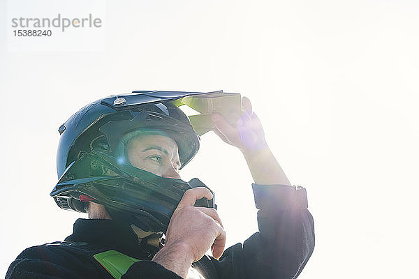 Porträt eines Motocross-Fahrers  der bei Sonnenuntergang einen Helm aufsetzt