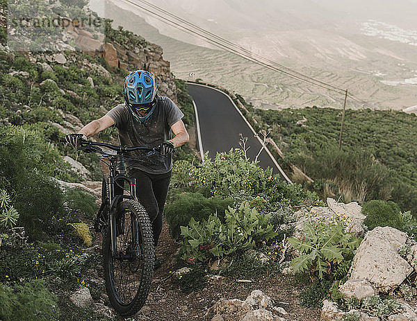 Spanien  Lanzarote  Mountainbiker  der sein Fahrrad in den Bergen schiebt