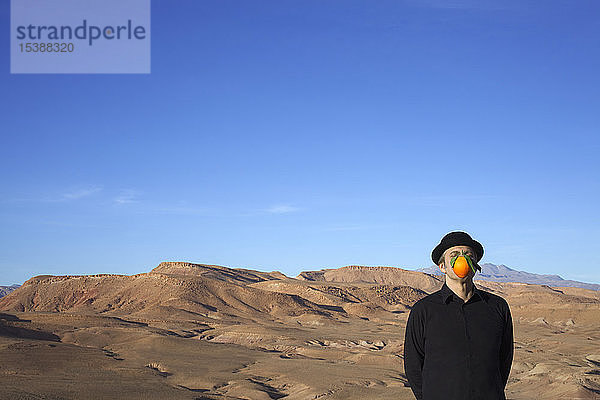 Marokko  Ounila-Tal  Mann mit Melone und einer orangefarbenen Mütze vor dem Gesicht