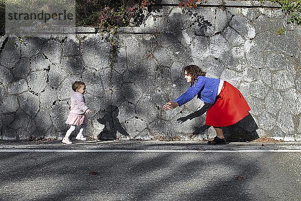 Kleines Mädchen rennt an einer Steinmauer zu seiner Mutter