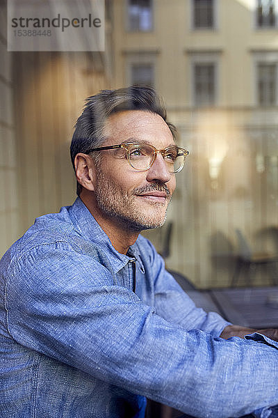 Porträt eines Brillenträgers hinter einer Fensterscheibe