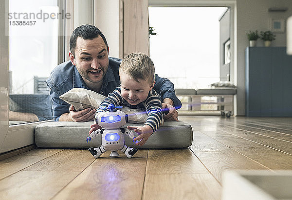 Aufgeregter Vater und Sohn liegen zu Hause auf einer Matratze und spielen mit einem Spielzeugroboter