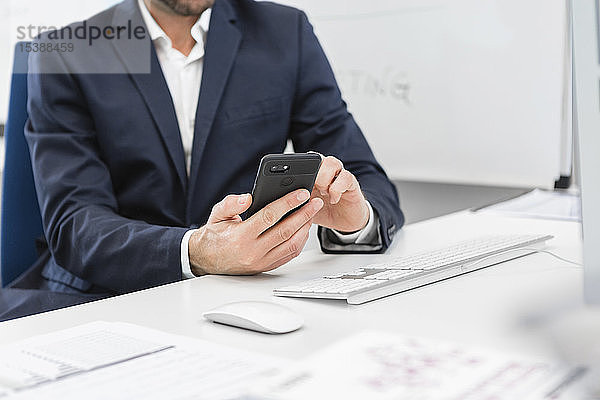 Nahaufnahme eines Geschäftsmannes  der am Schreibtisch im Büro sitzt und ein Mobiltelefon benutzt