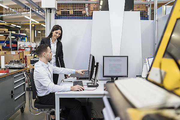 Geschäftsmann und Geschäftsfrau unterhalten sich am Computer in einer modernen Fabrik