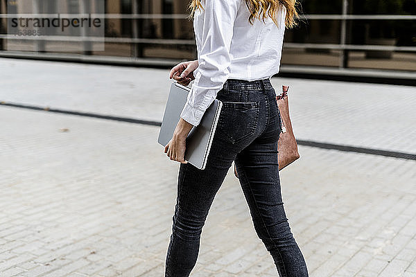 Junge Geschäftsfrau  die mit einem Laptop durch die Stadt läuft