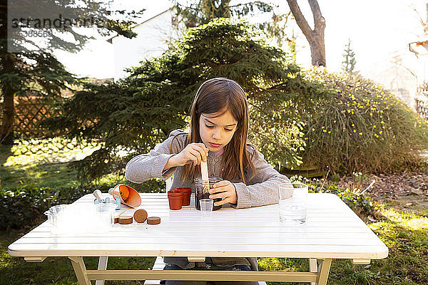 Porträt eines kleinen Mädchens am Gartentisch beim Säen von Samen