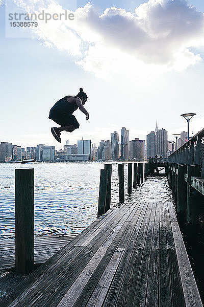 USA  New York  Brooklyn  junger Mann beim Parkour-Sprung vom Holzpfahl vor der Skyline von Manhattan