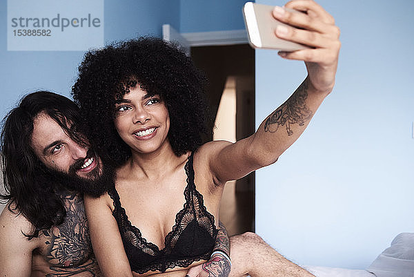 Glückliches  anhängliches junges Paar  das sich im Bett ein Selfie gönnt