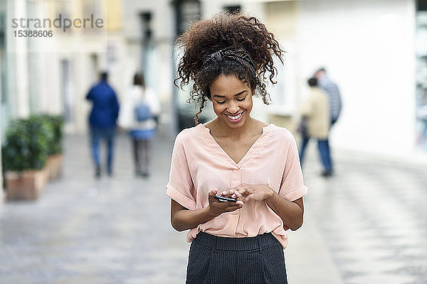 Lächelnde junge Frau benutzt Handy in der Stadt