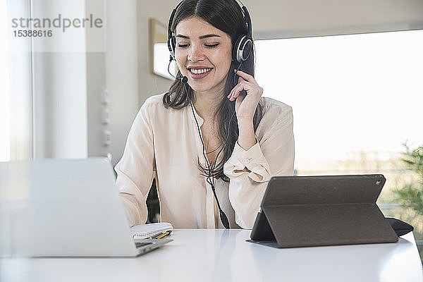 Junge Frau  die zu Hause am Tisch sitzt und ein Headset trägt