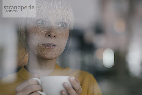 Bildnis einer schönen blonden Frau  die am Fenster steht und Kaffee trinkt