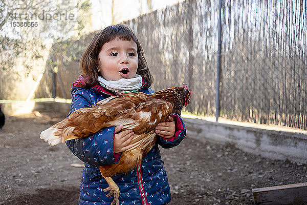 Porträt eines erstaunten Kleinkindes mit Huhn in der Hand
