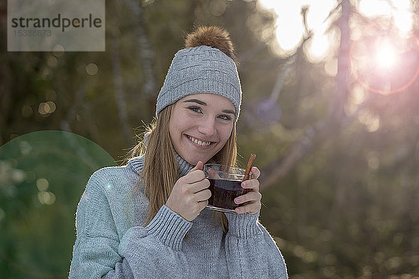 Porträt einer lächelnden jungen Frau mit einer Tasse Tee im Wald
