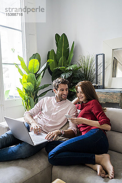 Mann und Frau sitzen auf der Couch  arbeiten am Laptop  benutzen ein Smartphone