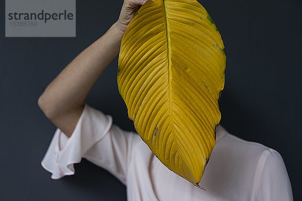 Frau bedeckt Gesicht mit einem gelben Bananenblatt