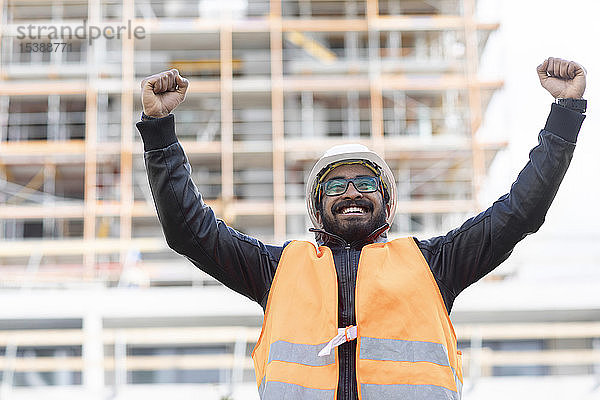 Porträt eines glücklichen Bauingenieurs vor der Baustelle mit Schutzhelm und Sicherheitsweste