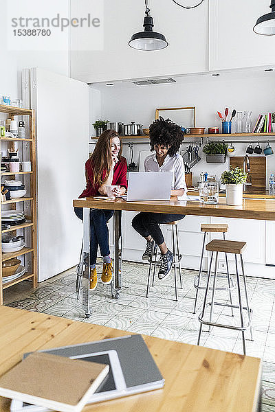 Zwei Frauen arbeiten gemeinsam in der Küche  benutzen einen Laptop und diskutieren über Dokumente