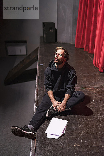 Probender Schauspieler sitzt mit Drehbuch auf der Theaterbühne