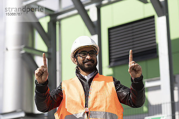 Porträt eines Bauingenieurs vor dem Kraftwerk mit Schutzhelm und Sicherheitsweste