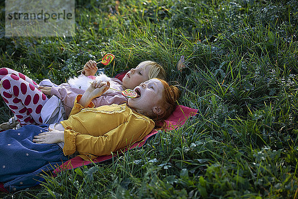 Zwei Schwestern liegen auf einem Feld und halten Lollipops