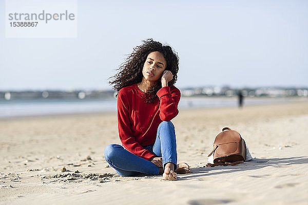 Nachdenkliche junge Frau sitzt am Strand