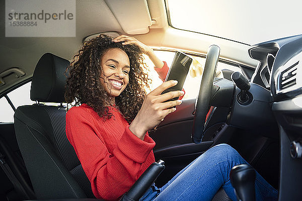 Glückliche junge Frau benutzt Handy im Auto