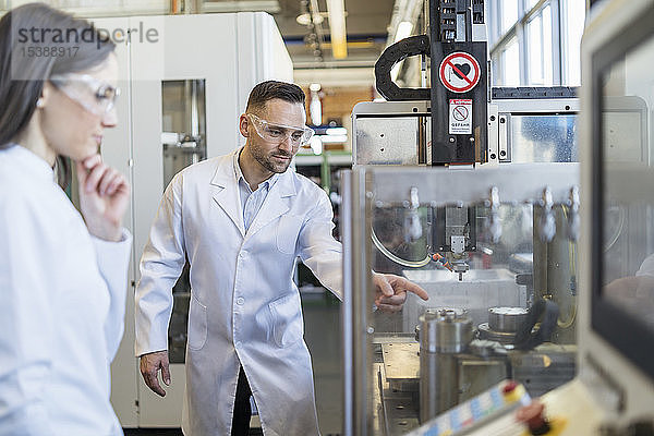 Kollegen in Laborkitteln und mit Schutzbrille beim Blick auf die Maschine in einer modernen Fabrik