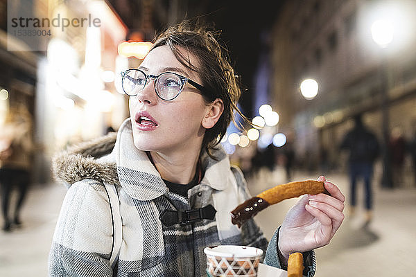 Spanien  Madrid  junge Frau in der Stadt  die abends typische Churros mit Schokolade isst