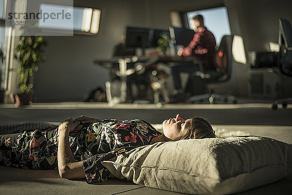 Frau macht ein Nickerchen  liegt auf einem Kissen auf dem Büroboden