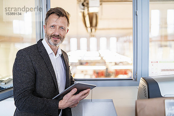 Porträt eines Geschäftsmannes mit Tablett am Fenster mit Fabrikhintergrund