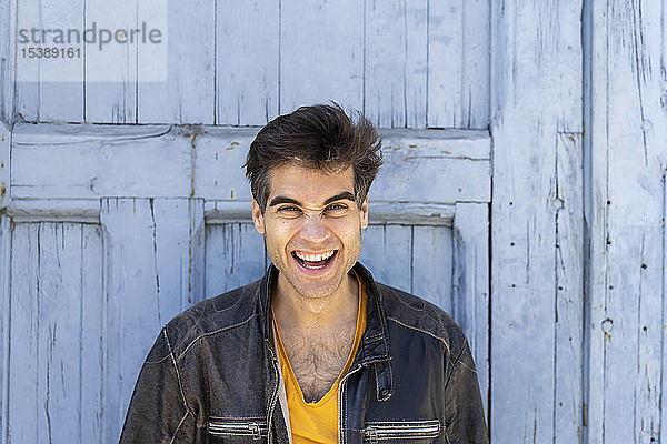 Porträt eines lachenden Mannes vor einer hellblauen Holztür