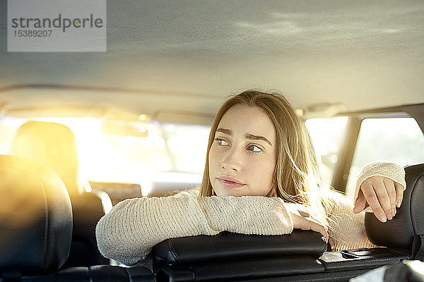 Junge Frau sitzt auf dem Rücksitz im Auto und schaut zur Seite