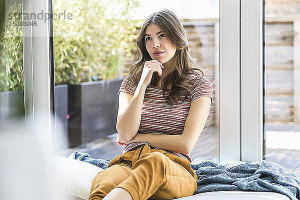 Nachdenkliche junge Frau sitzt zu Hause am Fenster