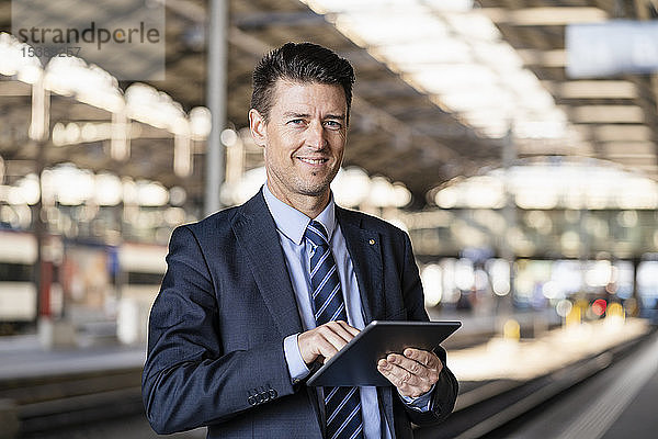 Porträt eines lächelnden Geschäftsmannes mit Tablette am Bahnhof