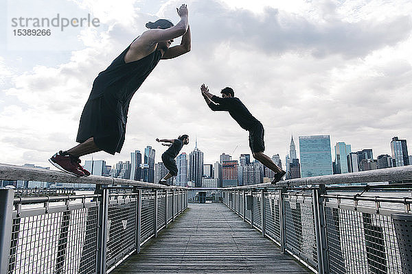 USA  New York  Brooklyn  drei junge Männer machen Parkour-Sprünge auf dem Pier vor der Skyline von Manhattan