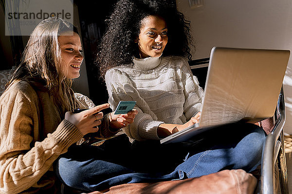Freunde sitzen auf der Couch  benutzen einen Laptop und bezahlen mit Kreditkarte