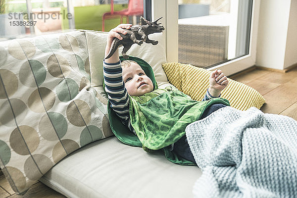 Junge in einem Kostüm auf einer Amateure liegend  der zu Hause mit einer Spielzeugfigur spielt