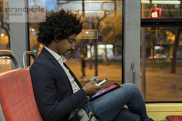 Spanien  Barcelona  Geschäftsmann nachts in der Straßenbahn mit Handy und Tablet