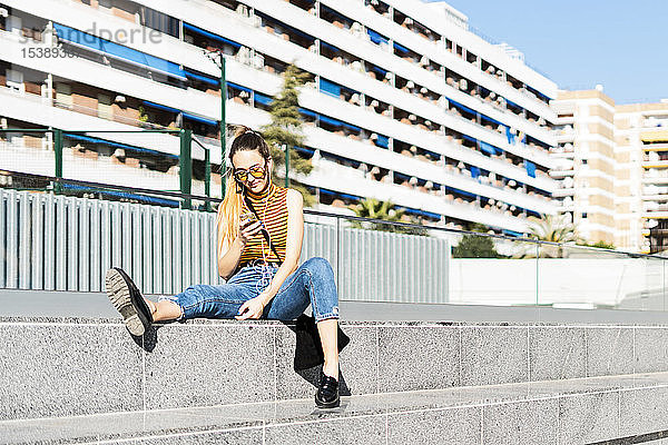 Spanien  Teenager-Mädchen mit Smartphone und Kopfhörern sitzt auf einer Treppe in der Stadt