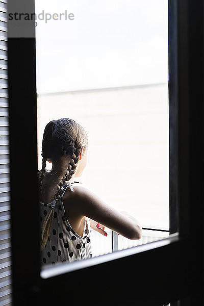 Rückansicht eines Mädchens in gepunktetem Kleid  das vom Balkon aus schaut